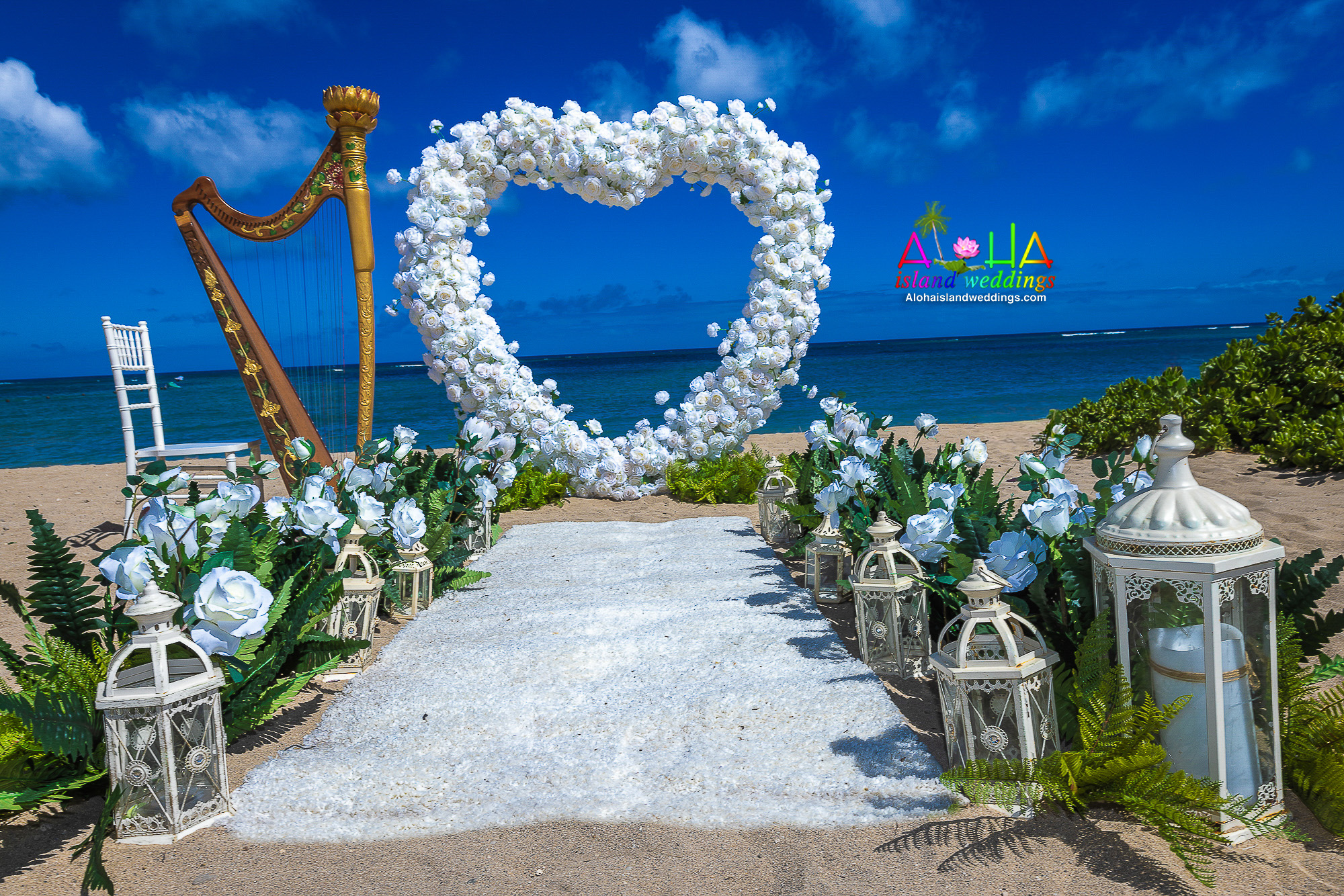 All-white rose heart with lanterns and a white carpet for a beach proposal